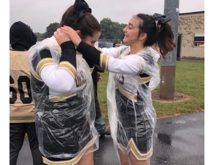 Cheerleader Hannah Sherinian helps Lexi Kelli into a raincoat before preforming at a football game.